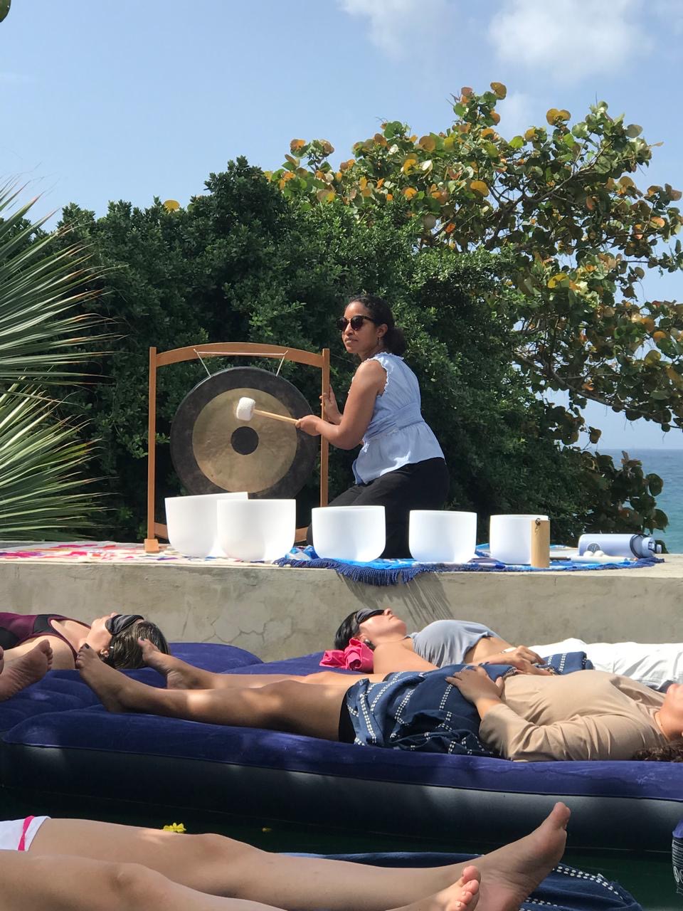 Marianne tocando el gong rodeada de cuencos de cuarzo en una sesión frente al mar